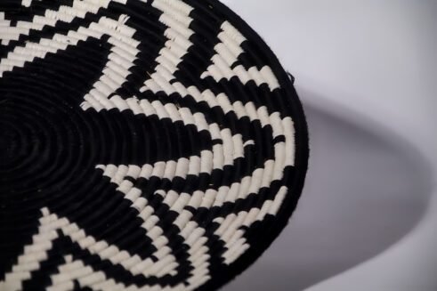 A handcrafted Moroccan coil basket featuring a bold black and white star pattern, placed on a neutral background with small stones surrounding it.