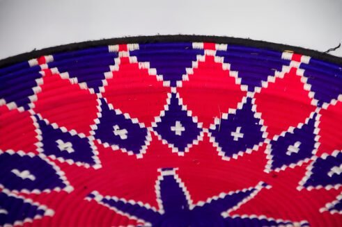 A handcrafted Moroccan coil basket with a vibrant pink and blue star design, surrounded by small stones on a neutral background.