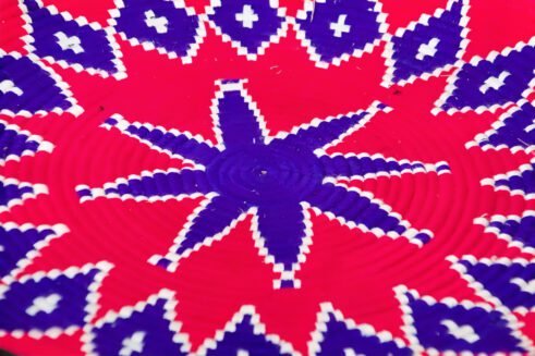 A handcrafted Moroccan coil basket with a vibrant pink and blue star design, surrounded by small stones on a neutral background.